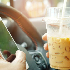 lady holding ice coffee and mobile phone in car