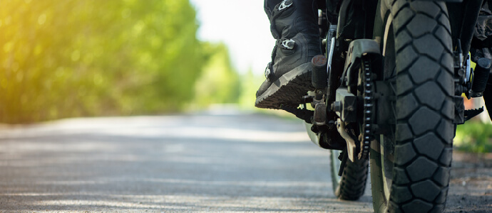 Motorbike wheel and biker leg in the boot close up on empty road, motorcycle accident injury