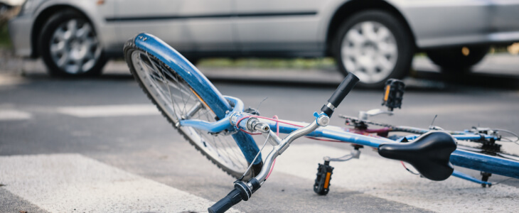 Blue bicycle laying in the road beside a silver sedan