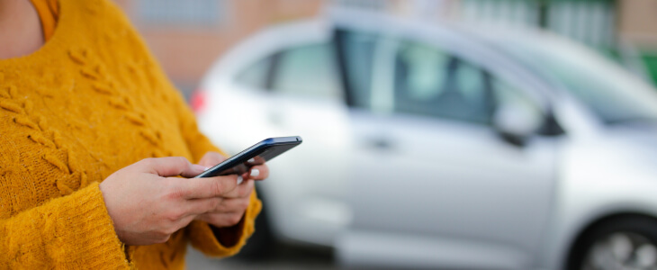 Person in yellow sweater using smartphone with parked car in background