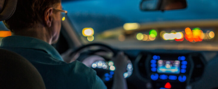 Driver at night with dashboard lights glowing and blurred city lights ahead