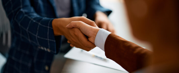 Two people in business attire shaking hands across a desk