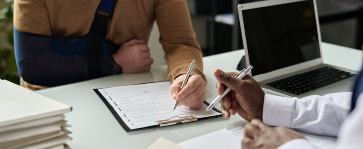 Injured client with arm sling reviewing and signing documents with lawyer