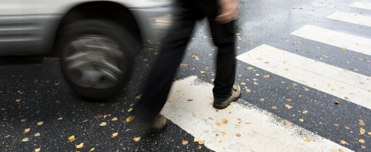 Car narrowly passing pedestrian on a crosswalk in rainy weather