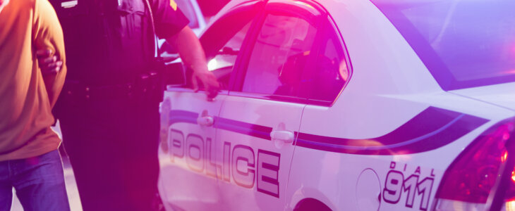 Police officer arresting a person beside patrol car with lights flashing