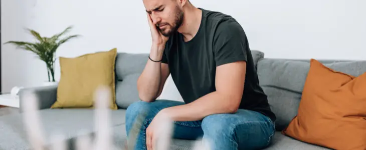 Man sitting on couch holding his face in pain, looking distressed