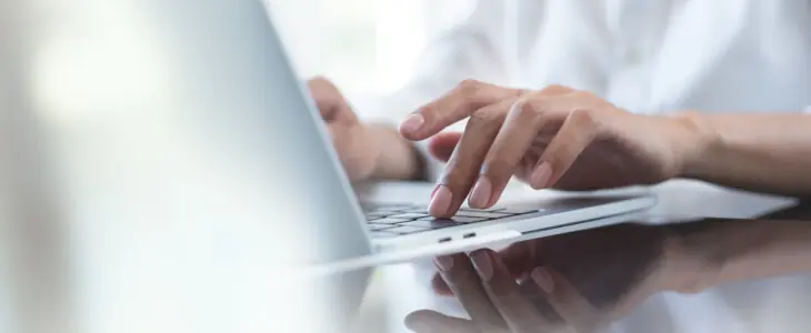 Close up of business woman hand typing on laptop computer keyboard with reflection on digital tablet on office table