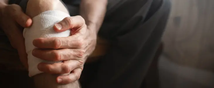 Close-up of person holding an injured, bandaged knee