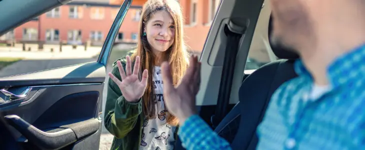 Father dropping off daughter at school, waving goodbye